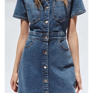 Jeansklänning med knappar - Snygg jeansklänning i blå denim med korta ärmar och knappar hela vägen framtill. Klänningen har två bröstfickor och markerad midja för en cool och avslappnad look. Perfekt för dig som gillar klassisk denimstil. Använd 1 gång 