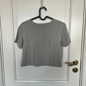 Grå croppad t-shirt från 157 - Enkel och stilren grå croppad t-shirt från 157 i 100% bomull. T-shirten har rund halsringning och korta ärmar, perfekt för en avslappnad och clean look. Passar dig som gillar basic plagg med modern twist.