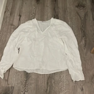 Vit blus med v-ringning - Säljer en stilren vit blus med v-ringad hals och långa ärmar. Blusen har en lätt och luftig känsla, perfekt för dig som gillar en enkel men fräsch look. Passar lika bra till jeans som till kjol.