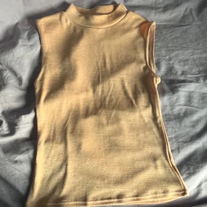 Beige ärmlös polotopp - Snygg beige polotopp med ärmlös design och hög hals. Toppen har en clean och enkel look som passar perfekt till jeans eller kjol. Mjuk och stretchig i materialet för en bekväm känsla hela dagen.