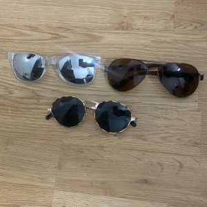 Tre olika solglasögon i coola stilar - Säljer tre par solglasögon: ett par med transparent båge och spegelglas, ett par klassiska pilotbågar med bruna linser och ett par runda glasögon med guldiga detaljer och svarta linser. Perfekta accessoarer för att lyfta din stil.