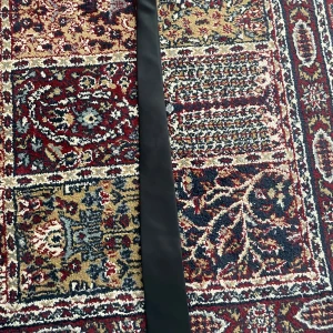 Svart slips från Dressmann - Snyggt svart bälte från Dressmann i satinliknande material. Bältet är brett och har en stilren, slät design utan spänne, perfekt för att ge en clean look till din outfit. Passar till kostymbyxor eller för att lyfta en skjorta.