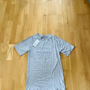 Grå Gymshark t-shirt med mönster - Snygg grå t-shirt från Gymshark med diskret mönster över hela tyget och logga på bröstet. Tillverkad i ett lätt och stretchigt material som passar perfekt för träning. Klassisk rund hals och korta ärmar för en sportig vibe.  ⚠️Denna vara är ej autentisk⚠️
