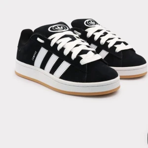Svarta Adidas Campus sneakers mocka - Klassiska Adidas Campus sneakers i svart mocka med vita ikoniska ränder och vit sula. Skorna har rund tå, platt gummisula och vita snören. Perfekt för dig som gillar retrostil och streetwear. Helt oanvända och fräscha🌼