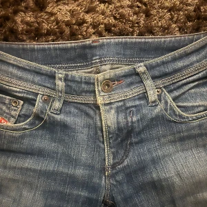 Blå low waist jeans från Diesel Industry - Säljer ett par klassiska blå jeans från Diesel Industry med snygga slitningar och kontrastsömmar. Jeansen har fem fickor, metallknapp och detaljerade nitar. Perfekta för dig som gillar en tidlös denimlook. Säljer pågrund av att dom är för tajta i midjan. 