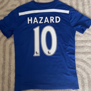 Hazard Chelsea 14/15 - Replika Chelsea tröja helt ny med tags med Hazard på ryggen. För fler bilder eller frågor tveka inte att skriva i dm. Fler tröjor i profilen. Se bio för tvätt anvisningar 