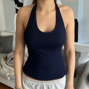 Mörkblå halterneck linnetopp - Snygg mörkblå halterneck linnetopp med knyt i nacken. Toppen är tight och figurnära med djup urringning och slät yta. Perfekt för dig som gillar enkel men stilren look.