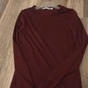 Mörkröd långärmad tröja 157 S - Enkel och stilren långärmad tröja från 157 i en snygg mörkröd färg. Tröjan har rund halsringning och är figurnära i modellen. Perfekt att matcha med jeans eller kjol för en clean look.
