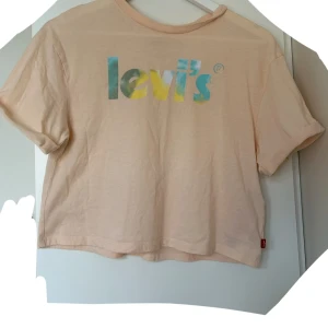 Levi's t-shirt - Snygg t-shirt från Levi's i ljusrosa med färgglatt logotryck framtill i blått, gult och grönt. T-shirten har korta ärmar och är tillverkad i mjuk bomull. Perfekt för en chill och avslappnad stil. I storlek 152cm (ca 10-12 år)