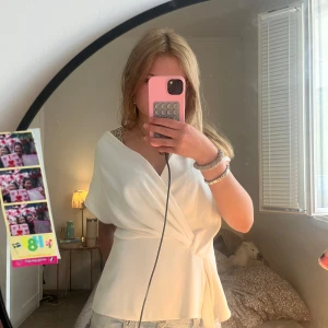 Vit omlottopp med knyt i midjan - Säljer en superfin vit omlottopp med knyt i midjan och v-ringad hals. Toppen har korta ärmar och en luftig, flowy passform som ger en chill och stilren vibe. Perfekt att styla med jeans eller kjol för en fräsch look.