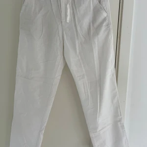 Vita linnebyxor från Zara med snörning - Snygga vita linnebyxor från Zara med avslappnad passform och dragsko i midjan. Byxorna har sidfickor och raka ben, perfekta för en chill och stilren look under varma dagar. Aldrig använda!