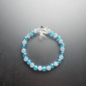 Blått och vitt pärlarmband med stjärna  - Snyggt armband med pärlor i blått och vitt, perfekt för dig som gillar unika detaljer. Armbandet har en genomskinlig berlock formad som ett stjärna. Elastiskt band gör det enkelt att ta på och av. Lite mindre I storleken