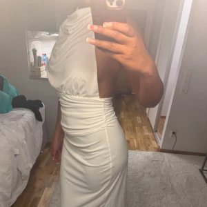 Vit långklänning från Zara - Säljer en elegant vit långklänning från Zara i storlek M. Klänningen har en asymmetrisk one shoulder-design, draperad överdel och öppen rygg.
