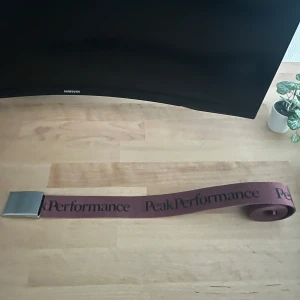 Vinrött Peak Performance bälte - Säljer ett vinrött tygbälte från Peak Performance med svart logotyp längs hela bältet. Bältet har en stilren, silverfärgad metallspänne som ger en clean look. Perfekt accessoar för att lyfta din outfit med en snygg look. Nypriset ligger på 500kr, priset kan diskuteras vid snabb affär! Hör av dig vi frågor!!