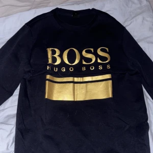 Svart tröja med guldtryck från Hugo Boss - Mörk blå långärmad tröja från hugo boss som helt ny använt den kanske 2-3 gånger de är en äldre model från 2021 och de är inga fel på den (nyskick) pris går att diskuteras 