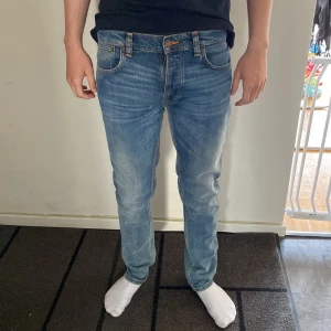 Blå jeans från Nudie Jeans - Säljer ett par klassiska blå jeans från Nudie Jeans med snygga slitningar och orange sömmar på bakfickorna. Modellen har normal passform och raka ben. Tillverkade i mjuk bomullsdenim med fem fickor och dragkedja. Perfekta för en avslappnad stil. Det är bara att höra av sig vid frågor och funderingar 😁