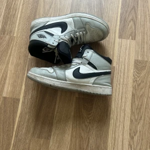 Nike Air Jordan 1 High vit/svart 39 - Snygga Nike Air Jordan 1 High sneakers i vitt och svart skinn med klassisk svart swoosh och högt skaft. Perforerad tå, vita snören och svart plös med Jumpman-logga. Perfekta för dig som vill ha en ikonisk streetstil.