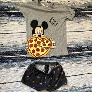 Grå Disney t-shirt med Mickey och pizza - Grå pyjamas från H&M x Disney med stort tryck av Musse Pigg som äter en pepperonipizza och texten 'Oh boy!!!' på bröstet. Klassisk passform med rund hals och korta ärmar. Tillhörande pyjamas shorts med pizzor på. Lågmidjade. Pris är diskuterbart och hör av dig om det är något!