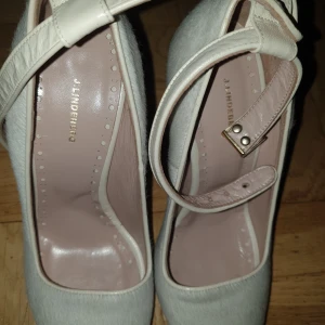 Vita pumps från J.Lindeberg, strl 37 - Snygga vita pumps från J.Lindeberg i storlek 37. Skorna har spetsig tå, hög klack med gulddetalj och justerbar rem runt vristen. Utsidan är klädd i ljust pälsliknande material och insidan i mjukt skinn. Perfekta för dig som gillar stilrena och unika detaljer.