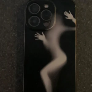 Svart mobilskal med konstnärligt motiv - Unikt svart mobilskal med konstnärligt tryck av en suddig, vit siluett av en kropp som trycker mot ytan. Skalet har en cool och modern vibe, perfekt för dig som vill sticka ut med din mobil. Passar till iPhone 13 Pro.