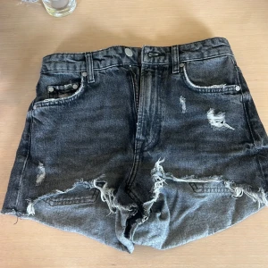 Grå slitna jeansshorts - Snygga grå jeansshorts med slitna detaljer och råa kanter. Klassisk femficksmodell med dragkedja och knapp framtill. Perfekta för en avslappnad och trendig look i sommar.