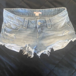 Ljusblå jeansshorts från Gina Tricot - Snygga ljusblå jeansshorts från Gina Tricot i storlek XXS. Modellen är lågmidjad med slitna detaljer, fransig kant och detaljer på fickorna både fram och bak. Använda en gång 