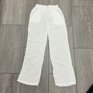 Vita linnebyxor från Chelsea Girls XS - Luftiga vita linnebyxor från Chelsea Girls med rak passform och resår i midjan. Byxorna har snörning framtill och sidfickor, perfekta för varma dagar. Tillverkade i Italien i ett tunt och svalt linnetyg.