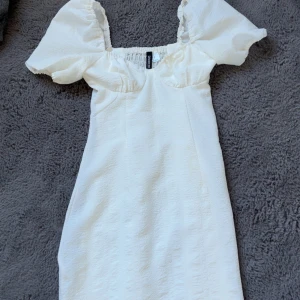 Vit klänning från H&M - Säljer en söt vit klänning från H&M med puffiga kortärmar och en smickrande passform. Klänningen har en dold dragkedja på sidan och elastisk smockdetalj i ryggen för extra komfort. Perfekt för sommarens alla tillfällen! särskilt skolavslutning o liknande🌼🤍