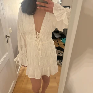 Studentklänning med volanger - Säljer en söt vit klänning med volanger och långa ärmar. Klänningen har en v-ringad design med snörning framtill och en härlig. Perfekt för studenten eller en speciell tillställning. 💫endast testad!