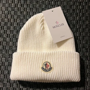 Vit ribbad mössa från Moncler - Snygg vit ribbad mössa från Moncler med broderad logotyp framtill. Perfekt för att hålla värmen under kyliga dagar. Stilren design som passar till det mesta.
