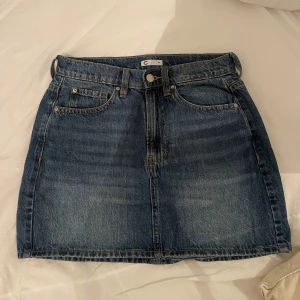 Jeanskjol  - Säljer en blå jeanskjol i rak modell, storlek M. Lagom längd, normal midja och med både fram- och bakfickor. Använd men i fint skick utan fläckar eller hål. Funkar lika bra till vardags som till en utekväll – enkel att styla med det mesta.