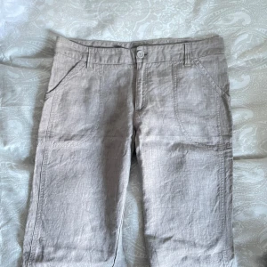 Beige linnebyxor - Snygga beige linnebyxor med normal passform. Byxorna har en klassisk design med knappar och dragkedja framtill samt fickor både fram och bak. Perfekta för en avslappnad stil.