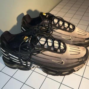 Nike tn sneakers - Snygga Nike Air Max sneakers i svart och grått med snörning och rund tå. Skorna har en unik design med synlig dämpning i sulan och små detaljer i vitt. Perfekta för både stil och komfort.