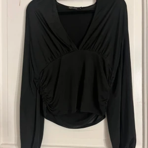 Svart långärmad topp från Nelly - Snygg svart långärmad topp från NLY One med en elegant v-ringning och draperade detaljer. Perfekt för en stilren look. Använd ett fåtal gånger. 