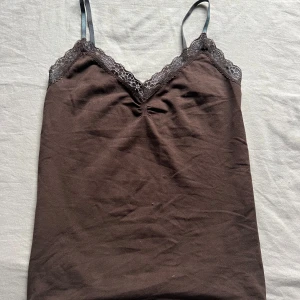 Brun linne med spetsdetaljer - Snygg brun linne med justerbara axelband och vacker spetskant vid halsringningen. Perfekt för lager-på-lager eller som ett stilrent basplagg. Pris kan diskuteras!💓