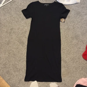 Svart ribbad klänning - Säljer en stilren svart ribbad klänning. Klänningen har korta ärmar och en enkel design som passar perfekt för olika tillfällen. Den är gjord i ett bekvämt material som ger en skön passform. Aldrig använd, storlek 170