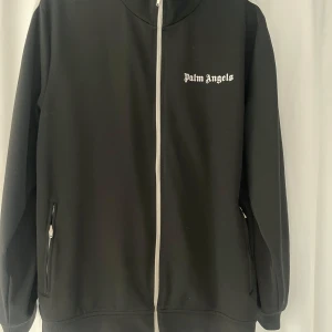 Svart track jacket från Palm Angels - Snygg svart track jacket från Palm Angels med vit dragkedja och logga på bröstet. Sitter som L