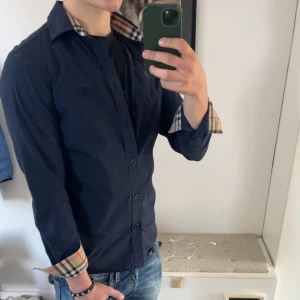 Mörkblå skjorta från Burberry - Säljer nu en riktigt fet skjorta från Burberry i färgen marinblå. Den är i toppen skick då det inte finns några defekter alls. Jag har kvitto på skjortan från Farfetch. Notera att det är spegeln som är smutsig och inte skjortan!! Nu pris är 4400 kr