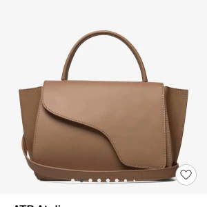 ATP ATELIER väska  - Elegant beige handväska med unik asymmetrisk design och stilrena linjer. Perfekt för att ge en sofistikerad touch till din outfit. Väskan har ett praktiskt handtag och en stilren look. Säljer eftersom jag vill köpa en ny väska, nypris: 5200-5800 . ATP väska . Skriv för egna bilder på den. Pris kan diskuteras. Färg hazelnut 