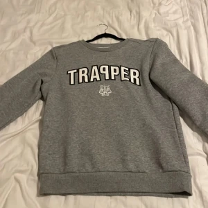 Grå trapper tröja - Säljer en grå sweatshirt med texten 'TRAPPER' tryckt på framsidan. Tröjan har långa ärmar och en rund halsringning. Perfekt för en avslappnad stil.