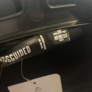 Svart bodysuit från Missguided - Säljer en snygg svart bodysuit från Missguided med djup urringning och krage. Den har långa ärmar och en figurnära passform. Perfekt för en stilren look.
