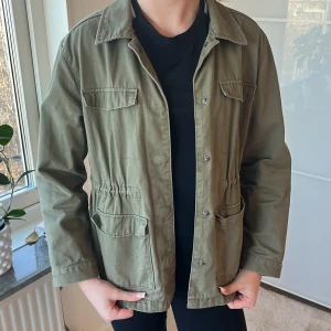 Olivgrön jacka från Kappahl - Säljer en mörkgrön jacka från Kappahl med knappar framtill och flera praktiska fickor. Den är i ett mycket bra skick!