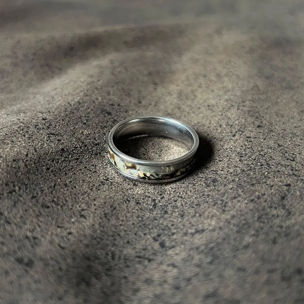 Otroligt vacker ring i stainless steel, prydd med äkta abalone-skal som fångar ljuset med sina levande färger. Varje ring är ett unikt konstverk, där havet och naturens egna mönster smälter samman i en tidlös design. En perfekt kombination av elegans och hållbarhet. Storlek US 10.75 (diameter: 20,5 mm, omkrets: 64,9 mm. Asusteet.
