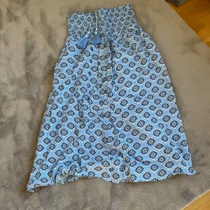 Mönstrad kjol från Gina Tricot - Säljer en blå och vit mönstrad kjol från Gina Tricot. Kjolen har en smockad midja och ett fint mönster med volangdetaljer. Perfekt för varma dagar!