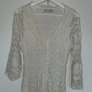 Vit klänning från Cream - Säljer en elegant vit klänning från Cream med ett subtilt mönster och knappar framtill. Klänningen har trekvartsärmar och en lätt transparent look, perfekt för en stilren outfit.