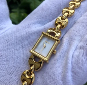 Guldfärgad klocka från Gucci - Elegant guldfärgad klocka från Gucci med en rektangulär urtavla och länkarmband. Urtavlan är vit med guldiga visare och märkeslogga. Perfekt som en lyxig accessoar för speciella tillfällen.
