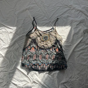 Mönstrad linnetopp med tunna axelband - Snygg och bohemisk linnetopp med tunna axelband och ett färgglatt mönster i jordnära toner. Perfekt för varma sommardagar eller festivaler. Toppen har en avslappnad passform 