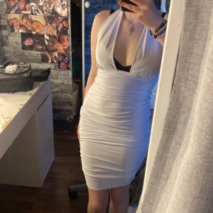 Vit klänning från Honor Gold - Snygg vit klänning från Honor Gold med djup v-ringning och öppen rygg. Klänningen är tight och kort, perfekt för en utekväll. Den har en elegant drapering och är ärmlös med halterneck-design.