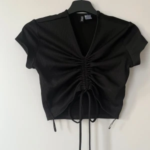 Svart ribbad topp från H&M - Säljer min svarta topp från H&M i storlek xs. Den har ett långt knytband som du kan vira runt midjan, en detalj som ger en elegant och feminin siluett.🎀