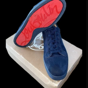 Blå sneakers från Christian Louboutin - Snygga blå sneakers i mocka från Christian Louboutin med den ikoniska röda sulan. Skorna har snörning och en rund tå, vilket ger en stilren look. Perfekta för dig som vill ha något unikt och trendigt.